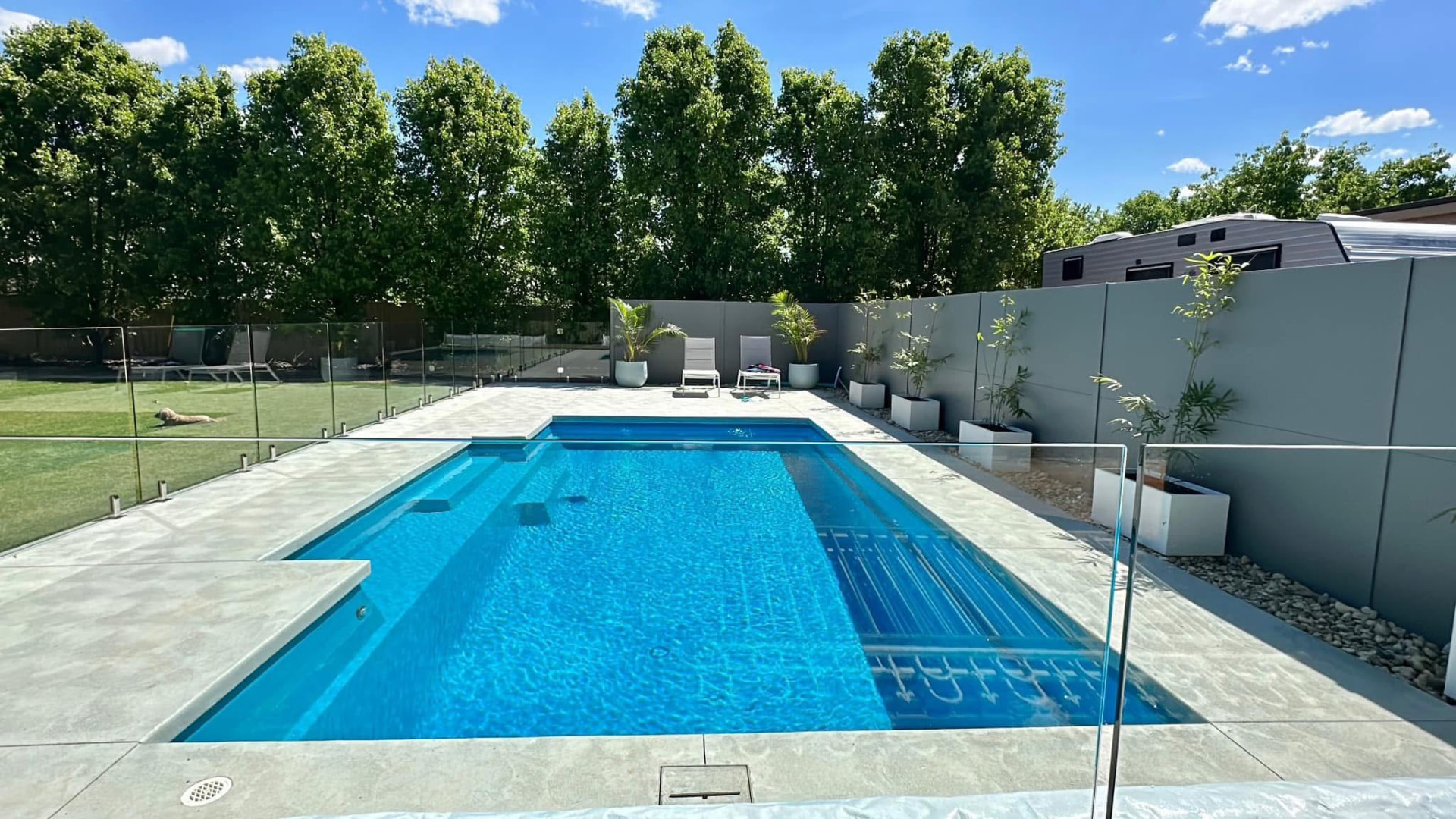 Finished concrete pool surround with glass fencing and landscaped backyard