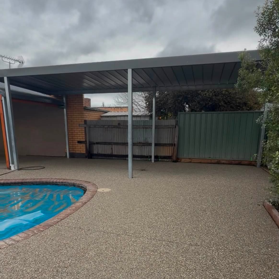 Finished exposed aggregate concrete pool surround around a backyard pool