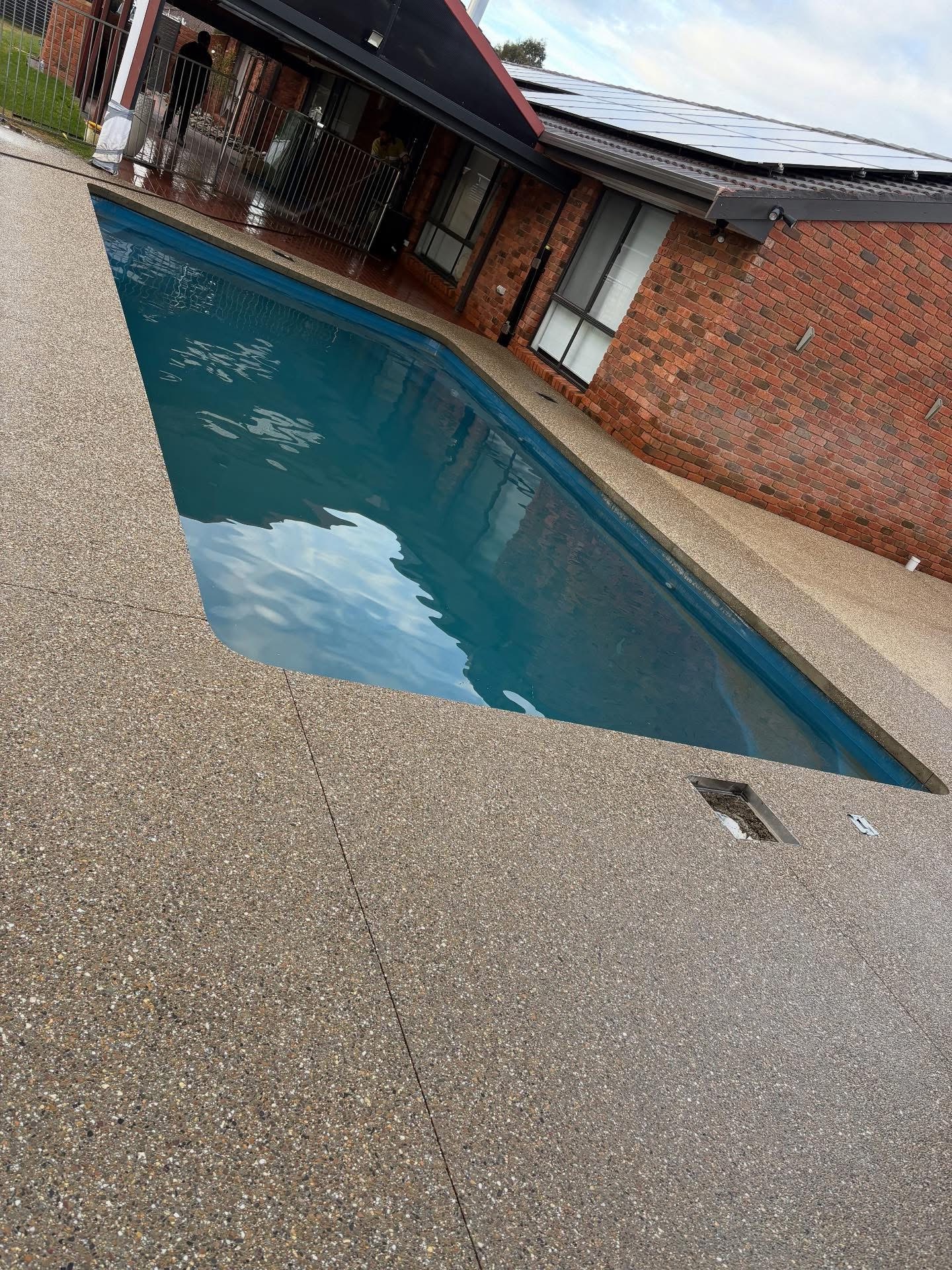 Exposed aggregate seamless edge pool surround around a backyard pool beside a brick home