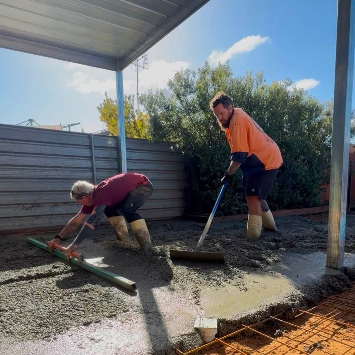 Crew screeding concrete over reinforcement mesh on a backyard slab